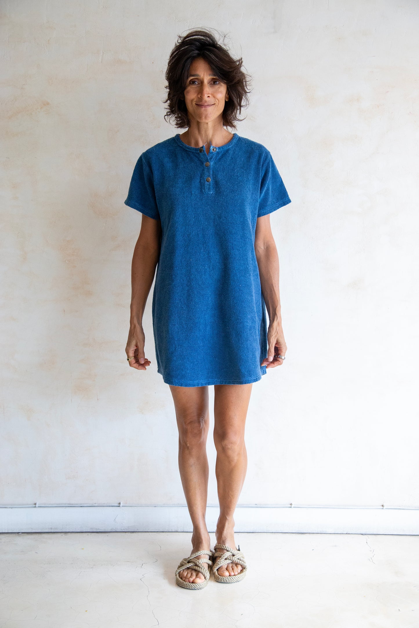 Woman wearing a blue dress standing against a plain white wall.