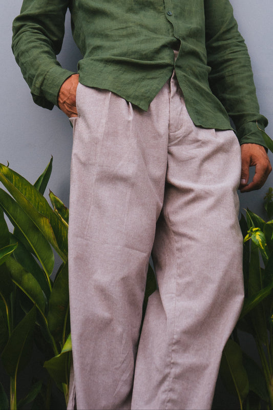 Man wearing a green shirt and beige pants standing against a gray wall with plants around.