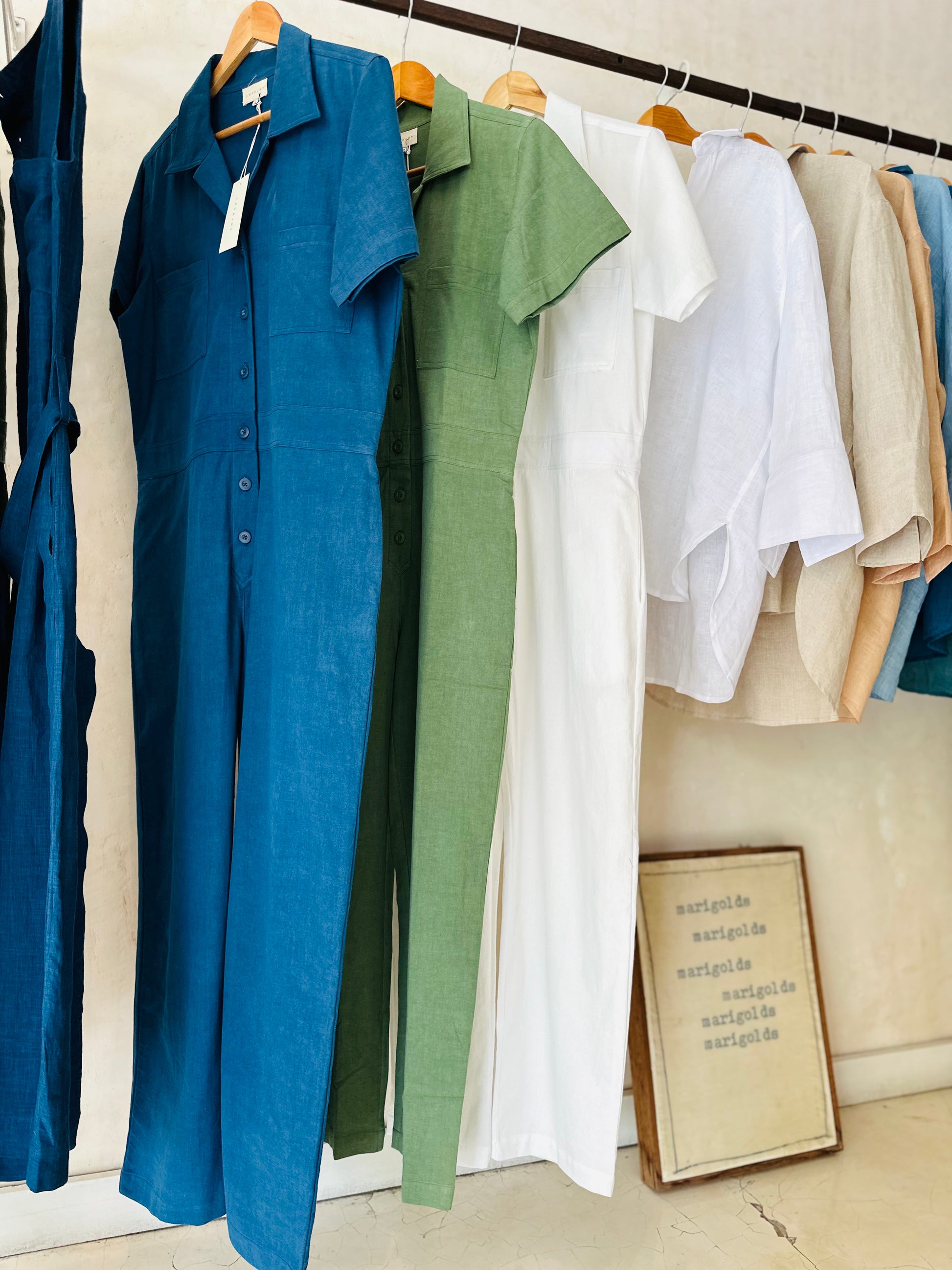 Playsuits hanging on a rack with a framed picture on the floor.