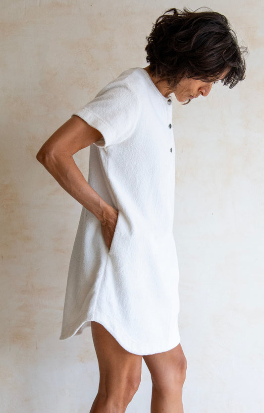 Person wearing a white dress standing against a plain wall.