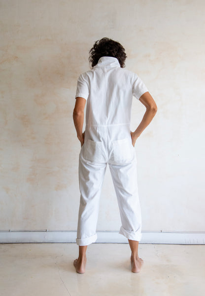 Person wearing a white outfit standing against a plain wall.